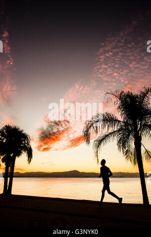 Silhouette eines Mannes läuft auf dem Bürgersteig der Beira Mar Norte Avenue bei Sonnenuntergang. Florianopolis, Santa Catarina, Brasilien. Stockfoto