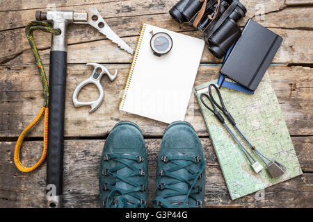 Klettern Sie Werkzeuge mit Stiefeln und Notebook auf hölzernen Hintergrund. Eis-Axt, Bergschuhe, Muttern, Kompass und Karte auf Holzbrett liegend Stockfoto