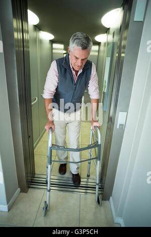 Senior woman walking mit Hilfe des Gehens Frame beim Abrufen aus dem Aufzug Stockfoto