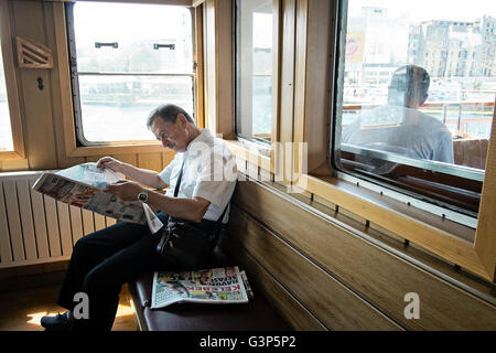 Ein Pendler liest eine Zeitung auf einer Fähre, wie es entlang des Bosporus in Istanbul, Türkei Reisen Stockfoto