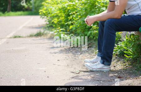 Junger Mann sitzt im Freien tragen Jeans. Stockfoto