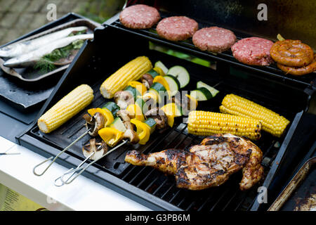 Spatchcock Huhn auf einem Grill mit Mais, Gemüse-Spieße, Burger und Würstchen gewickelt. Stockfoto