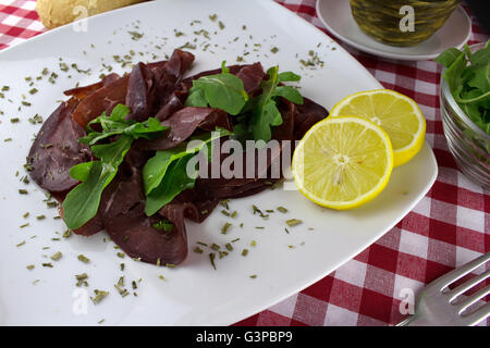 Scheiben vom luftgetrockneten Rindfleisch genannt Bresaola mit Rucola Salat, Olivenöl und Zitrone als typische italienische Vorspeise Stockfoto