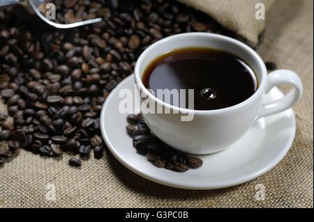 Tasse Kaffee ruht auf einer Leinwand Fläche neben einem Haufen von gerösteten Kaffeebohnen. Stockfoto