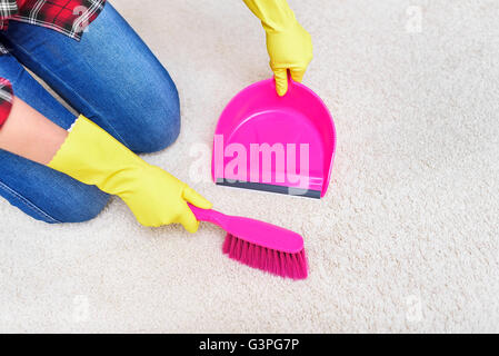 Weibliche Hände im gelben Handschuhe fegt eine Teppich-Bürste. Stockfoto