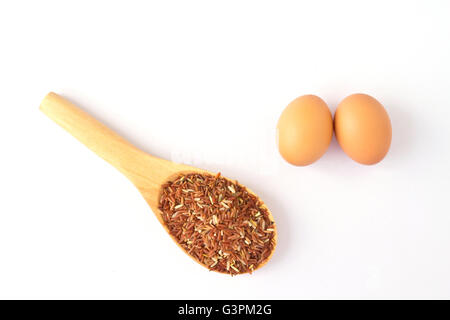 Braune Ei und Löffel aus Holz mit rotem Reis; auf einem weißen Hintergrund Stockfoto