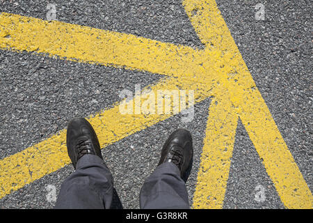 Männliche Füße in Lederschuhe stehen auf Asphaltdecke mit gelbe Markierungslinien, Egoperspektive Straße Stockfoto