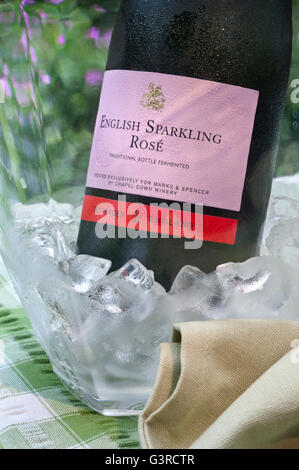 Englische funkelnden Rosé Wein Flasche in vereisten Weinkühler auf alfresco Picknick-Tisch mit Blumengarten hinter Stockfoto