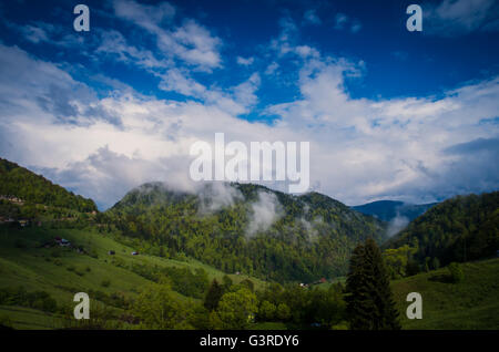 Landschaft mit alten Holzhäusern und Bergen von Wolken bedeckt. Berge und Wolken im Regenwald Stockfoto