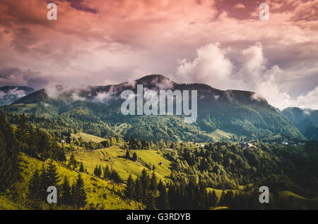 Landschaft mit alten Holzhäusern und Bergen von Wolken bedeckt. Berge und Wolken im Regenwald Stockfoto