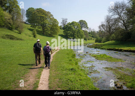 Ein älteres paar zu Fuß am Fluss in Bradford Dale in der Nähe von Youlgreave im Peak District, Derbyshire. Stockfoto