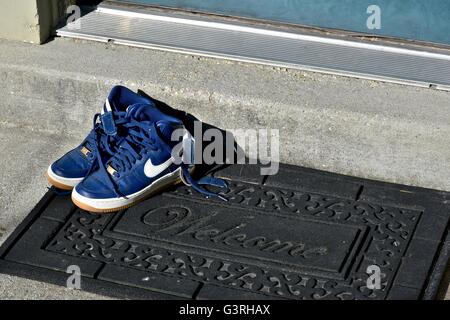 Ein paar blaue Nike Schuhe sitzen auf einer Fußmatte vor einem Haus Stockfoto