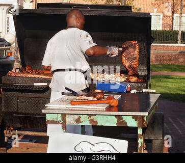 Ein dunkler dunkelhäutigen Mann bereitet verschiedene Fleischprodukte über ein Grill im Freien an einem sonnigen Tag. Stockfoto
