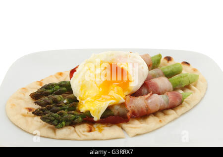 Nahaufnahme von Bauchspeck umwickelt Spargel mit einem flüssig Eigelb pochiertes Ei auf einem Fladenbrot Stockfoto