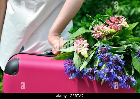 Mädchen stehen wieder mit einem rosa Koffer und Wildblumen Stockfoto