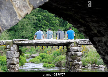 Blick durch einen Bogen des 18. Jahrhunderts Brücke über den East Dart River gegenüber Menschen sitzen auf dem alten clapper Bridge. Stockfoto