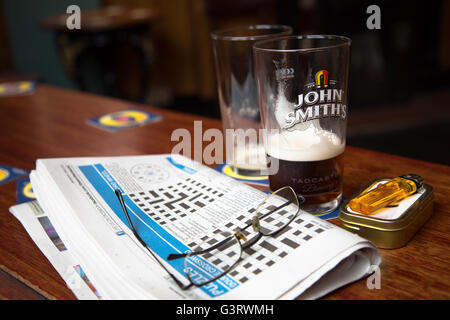 Ein Mittagessen Pause Blick auf die Tage lokale Kreuzworträtsel mit den Resten der ein Pint Bier/Ale in einem englischen Pub/Bar. Stockfoto