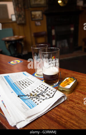 Ein Mittagessen Pause Blick auf die Tage lokale Kreuzworträtsel mit den Resten der ein Pint Bier/Ale in einem englischen Pub/Bar. Stockfoto