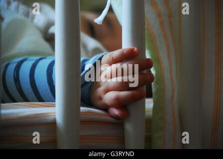 Schlafendes Baby in der Krippe Bar mit seiner Hand halten Stockfoto