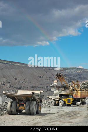 Muldenkipper mit Eisenerz auf den Tagebau geladen wird. Regenbogen in den Himmel im Hintergrund Stockfoto