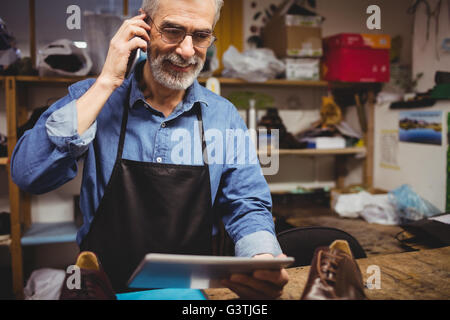 Schuster mit seinem Handy einzuberufen und abzuhalten einen Tabletcomputer Stockfoto