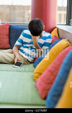 Aufgeregt junge auf Sofa sitzen und halten eines Handys Stockfoto