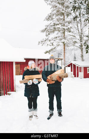 Jyväskylä, Finnland, Saakoski, junge Paar stehen und halten Brennholz mit Häusern im Hintergrund