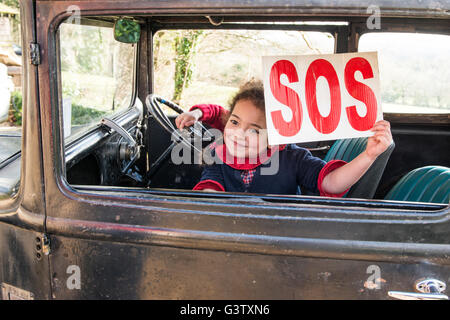 Ein junges Mädchen hält ein SOS-Zeichen in das Fenster eines Oldtimers. Stockfoto