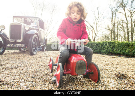 Ein vier Jahre alter Junge sitzt auf einer Spielzeug-Traktor vor einem Oldtimer. Stockfoto