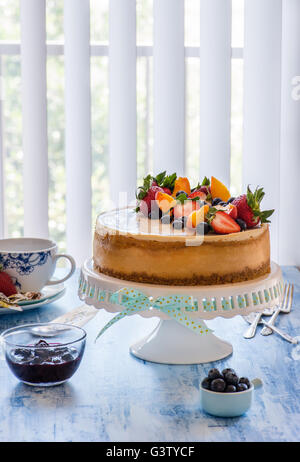 Karamell-Käsekuchen mit Lemon Curd auf Cakestand mit Heidelbeer-Sauce, dekoriert mit frischen Beeren. Tiefenschärfe, vertikale Stockfoto