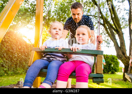 Vater treibt seine Töchter auf Schaukel in einem Park. Stockfoto