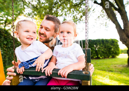 Vater treibt seine Töchter auf Schaukel in einem Park. Stockfoto