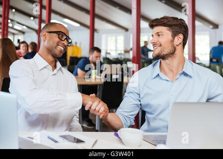 Zwei glückliche attraktive junge Geschäftsleute Händeschütteln und arbeiten im Büro Stockfoto