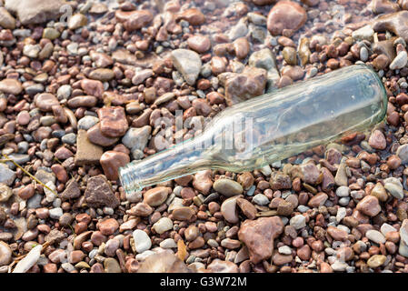 Einzigen leeren Klarglas Flasche auf den Steinen am Rande des Ufers. Stockfoto