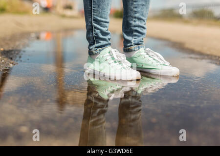 Frau im Sportschuhe in einer Pfütze stehen. Nahaufnahme der Füße in Wasser Stockfoto