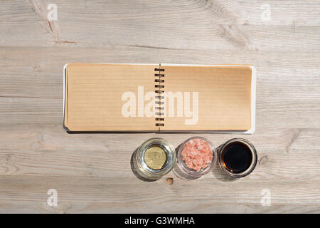 Leere offene Notebook für Notizen und Pfeffer, Lorbeer, Rosmarin, Zwiebeln, Salz, Olivenöl, Soja-Sauce auf einem Holztisch Stockfoto