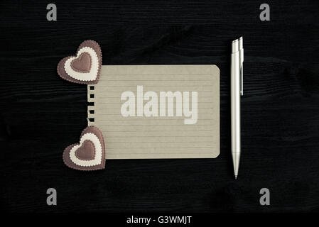 Ein leeres Blatt Papier, Stift und zwei Herzen auf einem hölzernen Hintergrund. Foto im Vintage-Stil Stockfoto