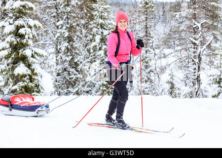 Junge Frau Langlauf mit Pull hinter Baby Pulk Schlitten Stockfoto