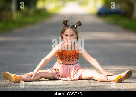 Fröhliches kleines Mädchen sitzt auf der Straße. Stockfoto