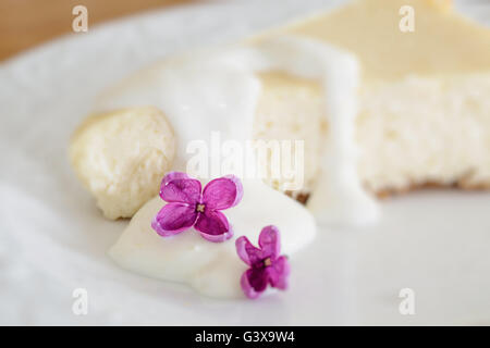 Zitronen-Käsekuchen mit einzelnen lila Blüten verziert. Absichtliche geringe Schärfentiefe mit Fokus auf die lila Blume. Stockfoto