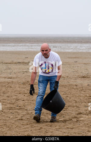 Mann hilft, klare Wurf und anderem Müll von einem Sandstrand entfernt in Lytham St. Anne's, Lancashire, UK Stockfoto