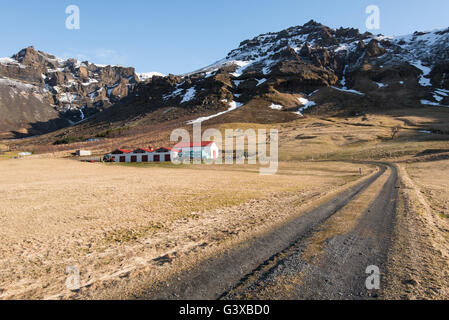 Countryroad führt zu einem typischen isländischen Bauernhaus unter den Bergen mit Schnee in Island bedeckt Stockfoto