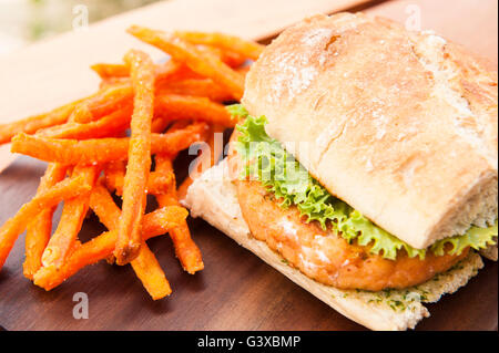 Lachs-Burger mit Salat und Pesto-Sauce mit Süßkartoffel Pommes frites serviert Stockfoto