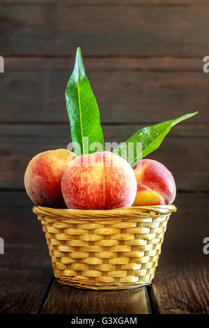 Pfirsiche in geflochtenen Korb auf dunklem Holz. Textfreiraum Stockfoto