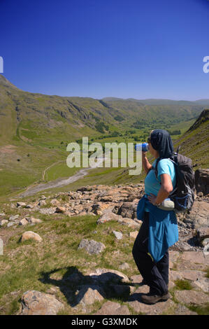 Lady Wanderer trinken aus der Flasche blickte Langdale Tal von Braun Howe in Lake District National Park, Cumbria, England Stockfoto