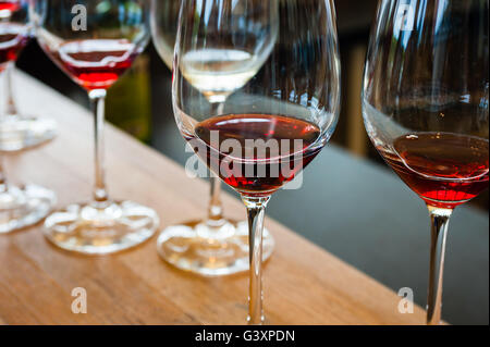 Detail der Weingläser mit roten Wein Proben, auf hölzernen Theke mit anderen Gläsern im Hintergrund. Stockfoto
