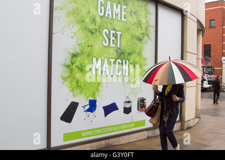 Wimbledon London, UK. 16. Juni 2016. Fußgänger in Regenschirme bergende gehen vorbei an eine große Tennis-Plakat mit den Worten "Spiel und Spiel" als Wimbledon bereitet Gastgeber der 2016 Rasenplatz Tennis Championships Credit: Amer Ghazzal/Alamy Live-Nachrichten Stockfoto