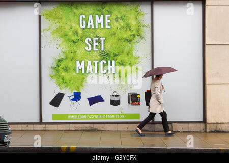 Wimbledon London, UK. 16. Juni 2016. Fußgänger in Regenschirme bergende gehen vorbei an eine große Tennis-Plakat mit den Worten "Spiel und Spiel" als Wimbledon bereitet Gastgeber der 2016 Rasenplatz Tennis Championships Credit: Amer Ghazzal/Alamy Live-Nachrichten Stockfoto