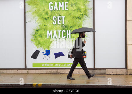 Wimbledon London, UK. 16. Juni 2016. Fußgänger in Regenschirme bergende gehen vorbei an eine große Tennis-Plakat mit den Worten "Spiel und Spiel" als Wimbledon bereitet Gastgeber der 2016 Rasenplatz Tennis Championships Credit: Amer Ghazzal/Alamy Live-Nachrichten Stockfoto