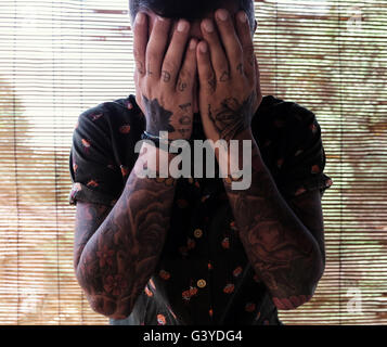 Mann mit Tattoos bedeckte sein Gesicht mit den Händen Stockfoto